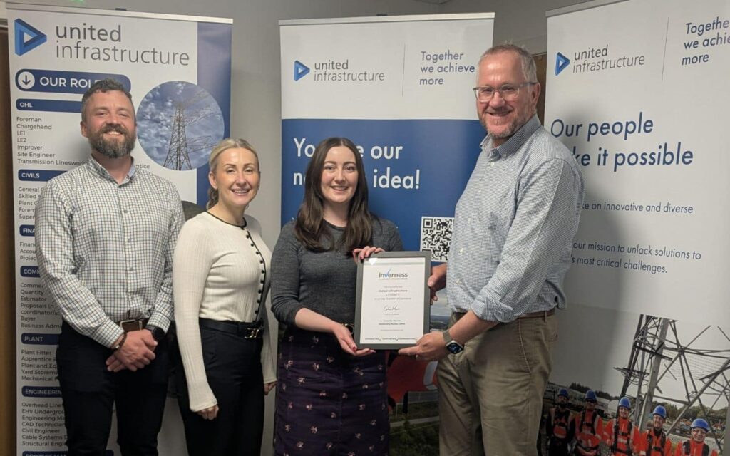 united infrastructure colleagues stand in front of pull up banners holding inverness chamber partnership partnership award