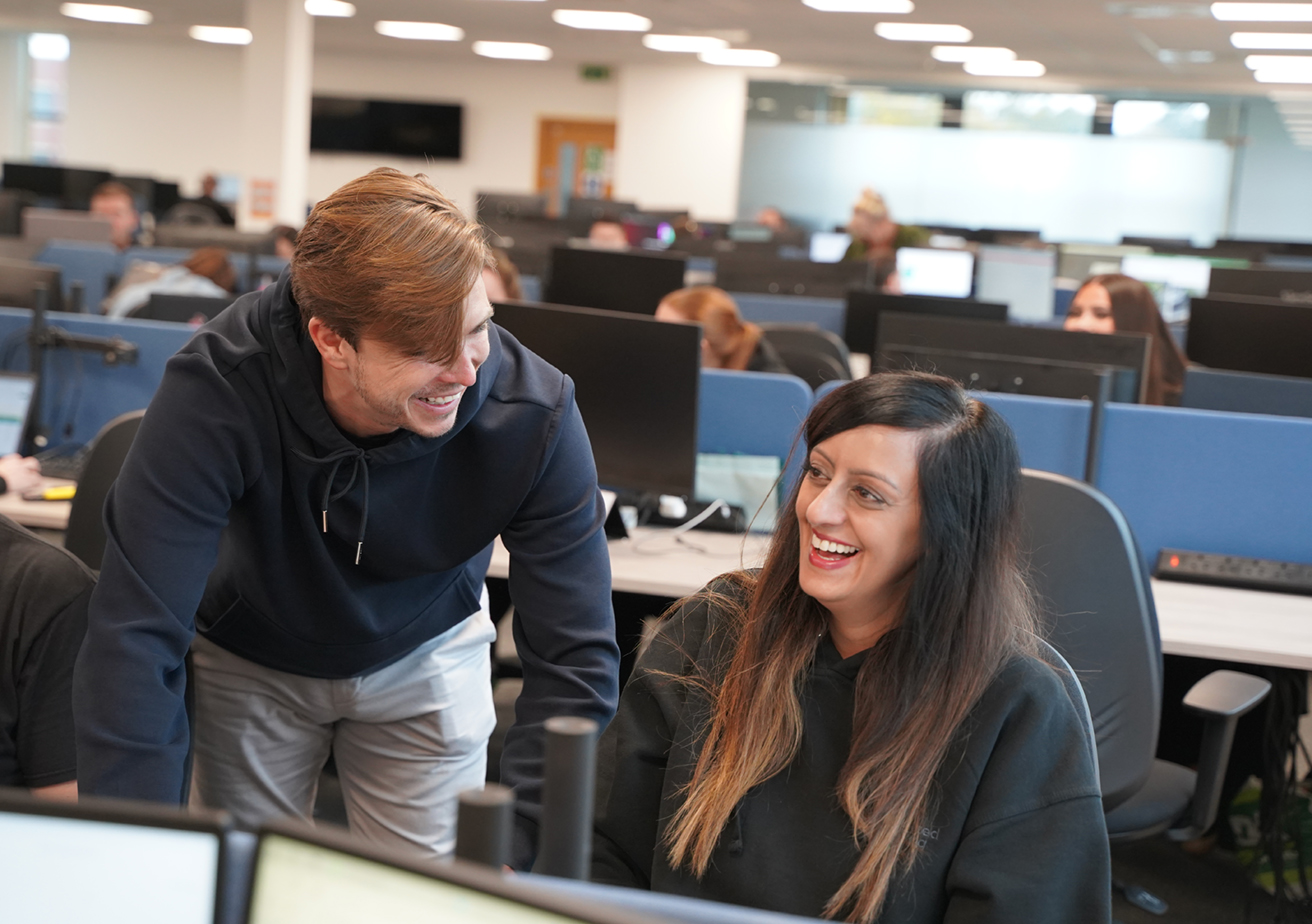 TWO EMPLOYEES AT DESK TALKING AND LAUGHING