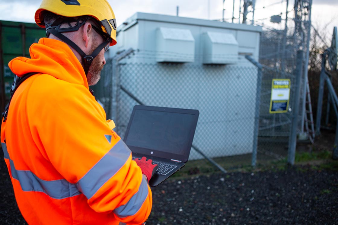 employee working on laptop in front of telecoms tower