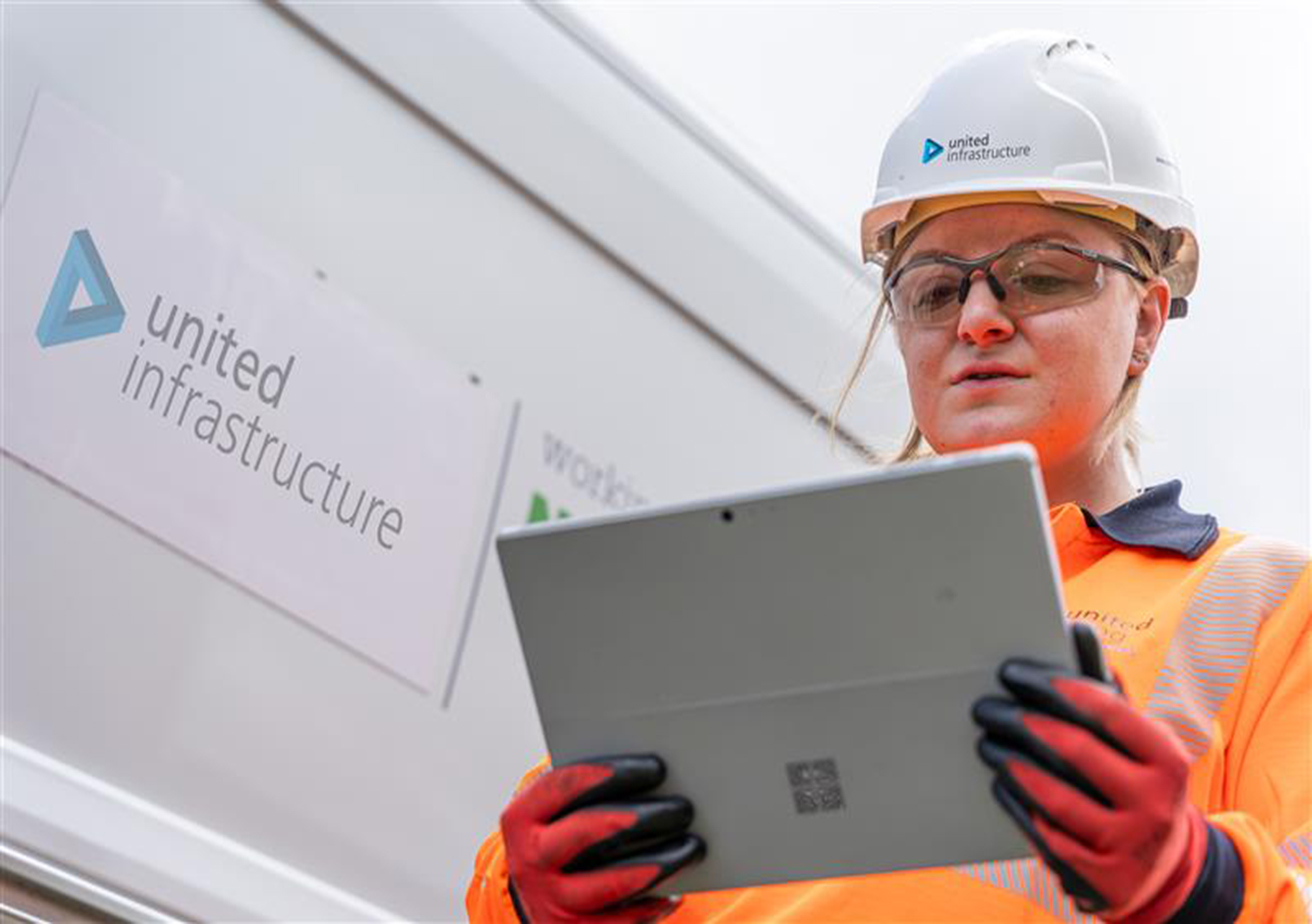 United infrastructure employee holding tablet standing in front of branded van