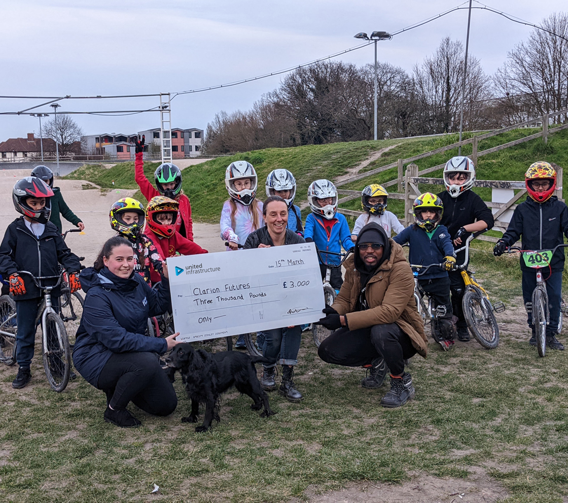 united infrastructure employees holding cheque with children in park on bikes