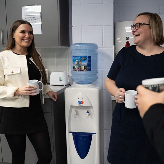 two employees standing in company kitchen chatting and laughing