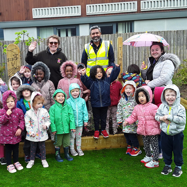 united infrastructure employees and school children standing outside in a garden