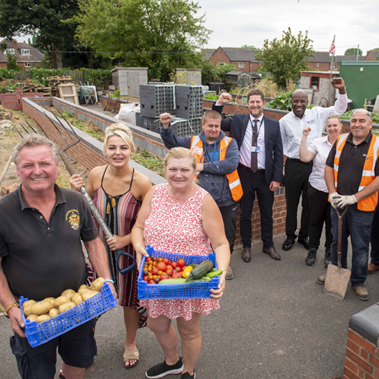 group of employees standing together holding spades and baskets of vegetables