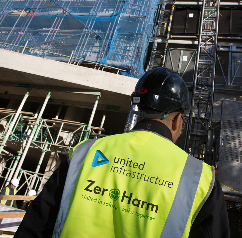 back of united infrastructure employee looking up at high rise building with scaffolding
