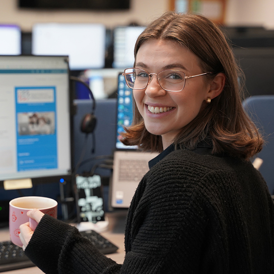 united infrastructure sat at desk holding coffee mug and smiling
