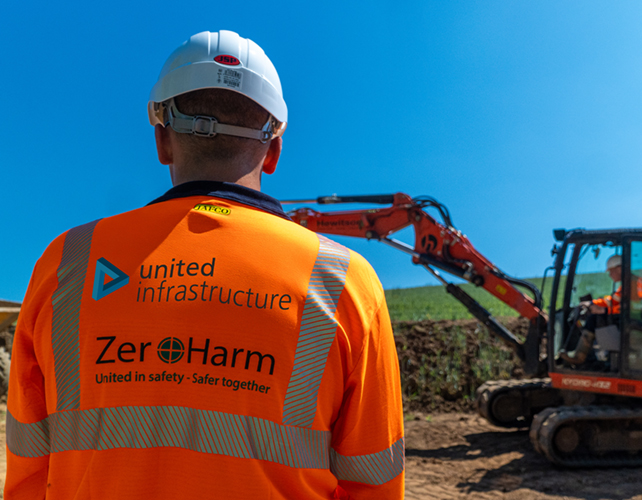 united infrastructure employee on site wearing ppe in front of excavator