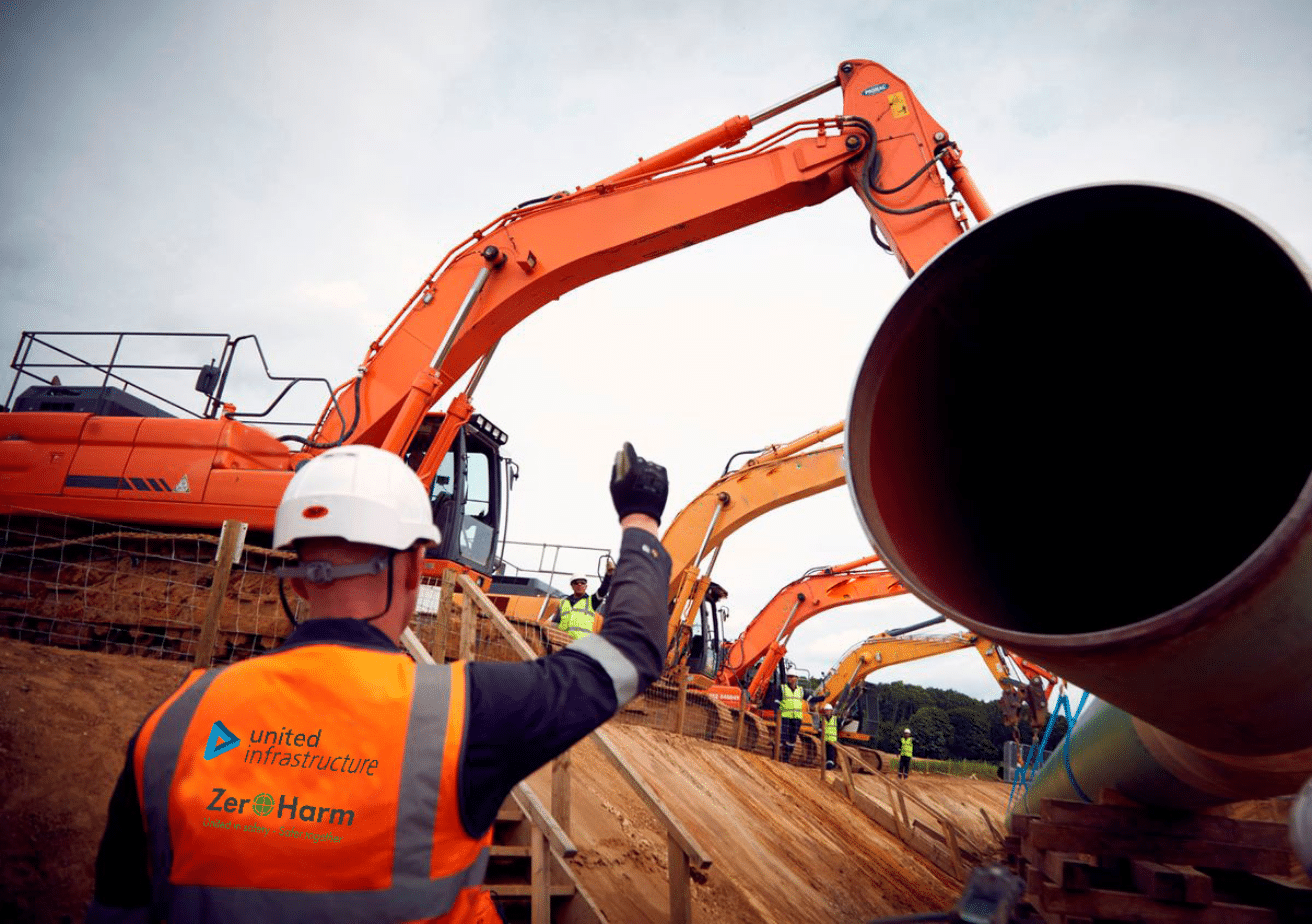 united infrastructure employee instructing installation of large gas pipe into ground